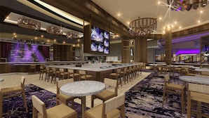 A spacious bar area with multiple seating options, a large screen displaying a concert, and a modern chandelier.
