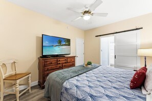 A bedroom with a bed, a TV on a wooden dresser, a ceiling fan, and a door. - Atlantis Villas 104 -Renovated 6 BR-Game Room-Pool (NORTH MYRTLE BEACH)