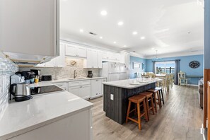 Una cocina moderna con armarios blancos, una isla central con taburetes y un comedor con paredes azules y muebles de madera.