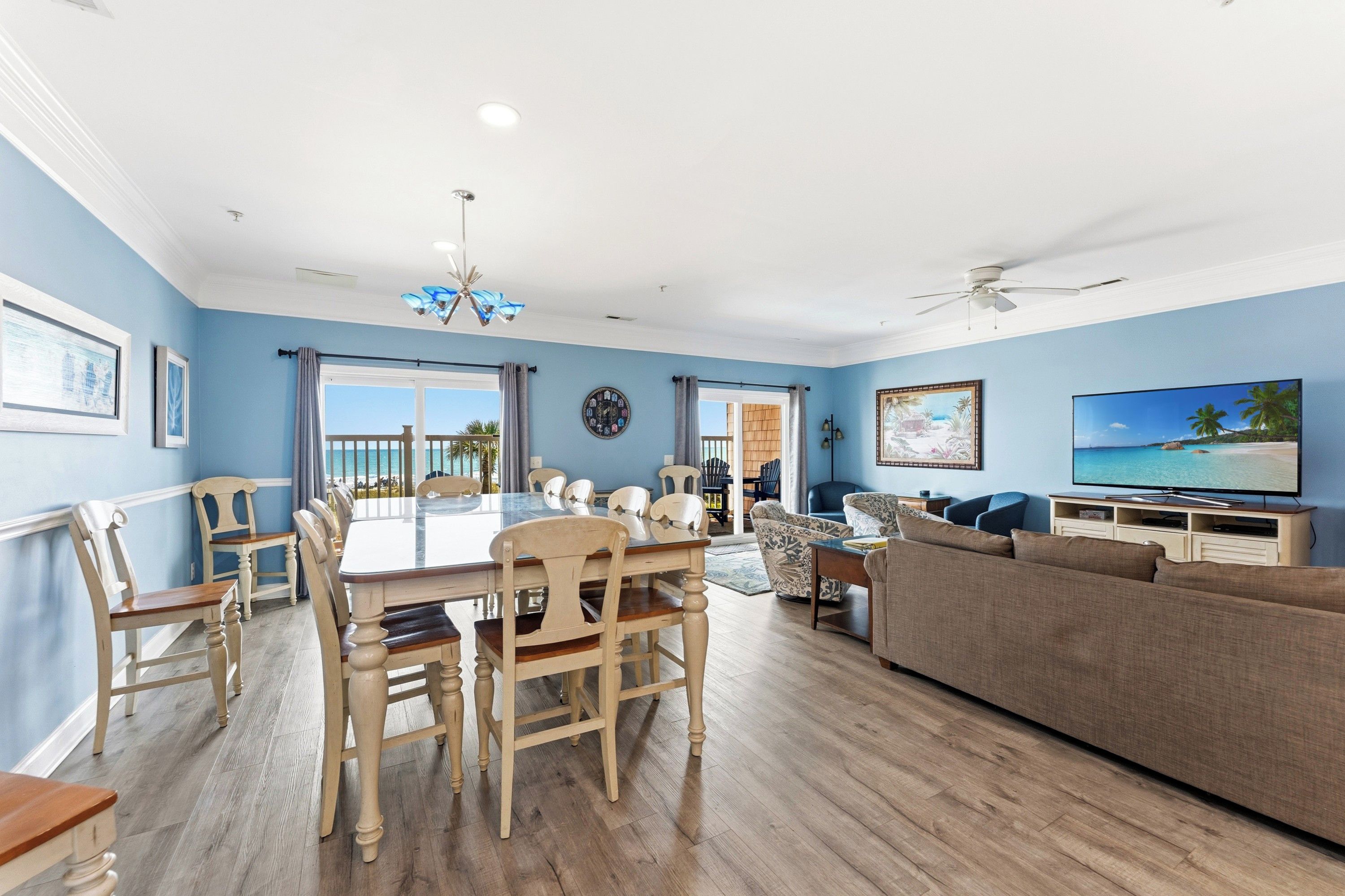 A spacious living room with a dining area, a large flat-screen TV, and a balcony with a view.