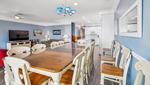 A dining area with a wooden table and white chairs, a ceiling fan, and a modern chandelier.