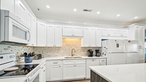 A modern kitchen with white cabinetry, a microwave, a coffee maker, and a refrigerator.
