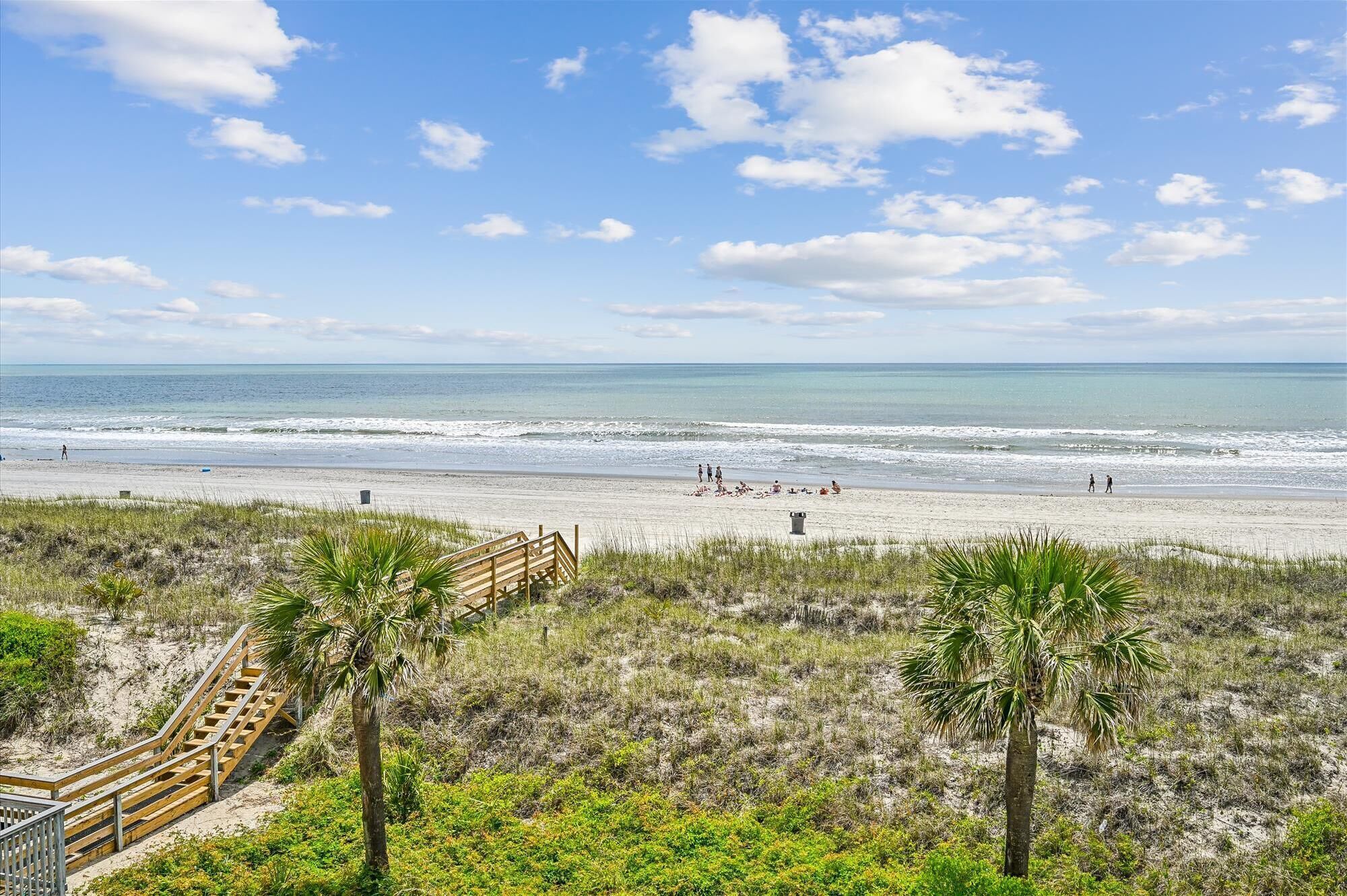 A beach with a wooden staircase leading down to the sand, palm trees, and the ocean.