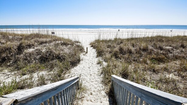 A sandy beach path leading to the ocean, flanked by grassy dunes.