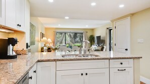 Een moderne keuken met witte kasten, granieten aanrechtbladen, een inbouwspoelbak en een eethoek met een tafel en stoelen.