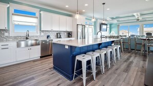 Una cocina moderna con una isla central, armarios blancos, electrodomésticos de acero inoxidable y taburetes de bar.