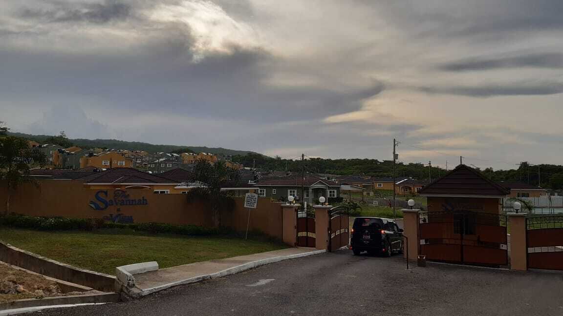 Una entrada protegida por un portón a una zona residencial con casas y un cartel que dice 'Savanah Village'.