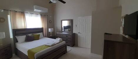 A bedroom with a bed, bedside tables, a dresser, a mirror, a ceiling fan, and a TV.