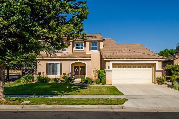 A two-story house with a front garage, a well-maintained lawn, and a large tree to the left.