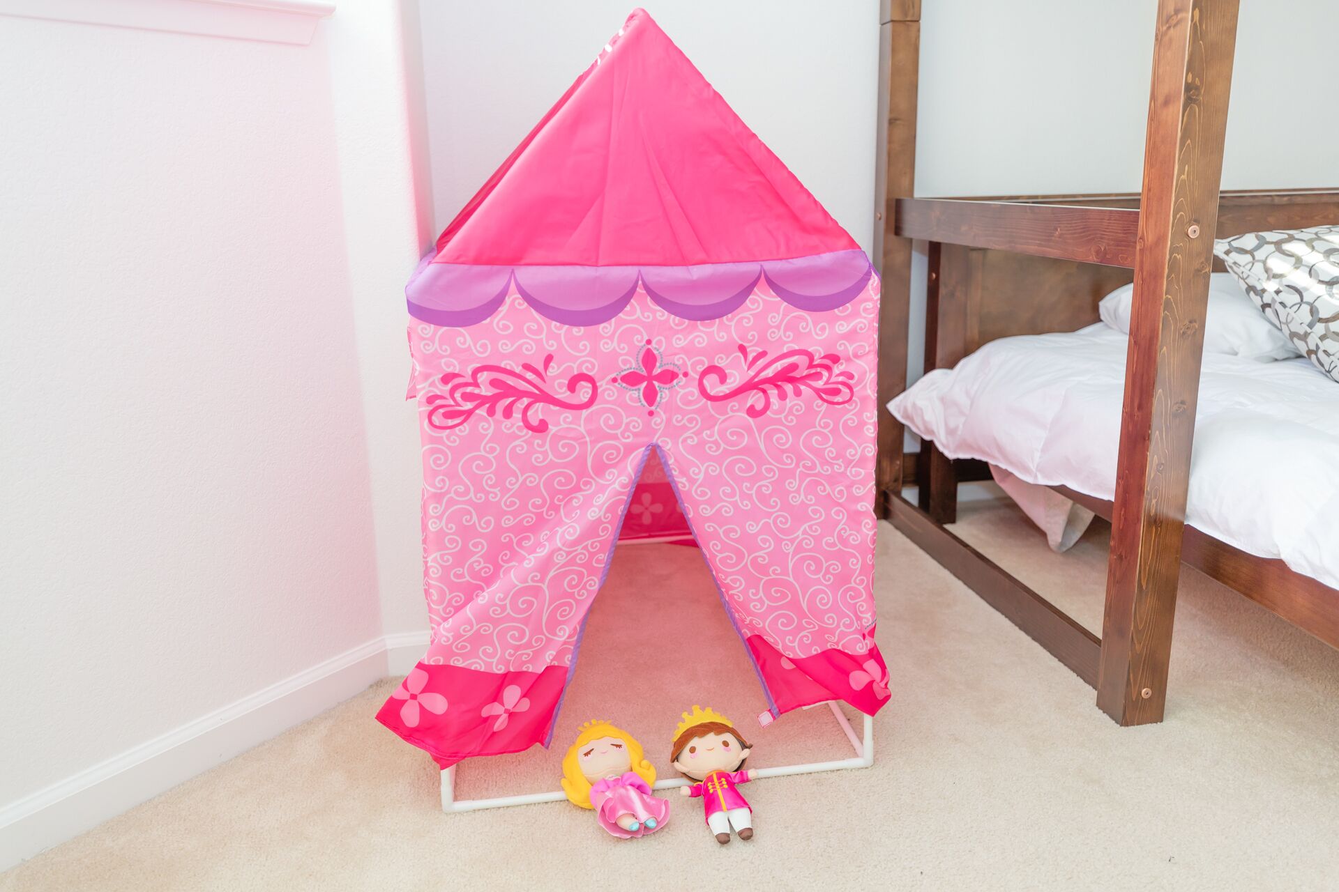 Une chambre avec un lit superposé, une structure rose en forme de tente et deux poupées sur le sol.