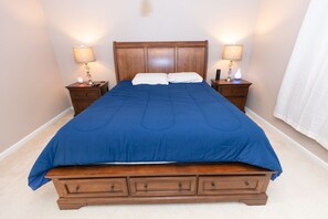 A bedroom with a large bed, wooden headboard, two bedside tables with lamps, and a white curtain.