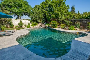 A swimming pool with a curved edge, surrounded by a stone deck and various plants.