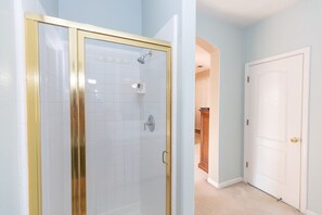 A bathroom with a glass shower enclosure, white tiled walls, and a white door.