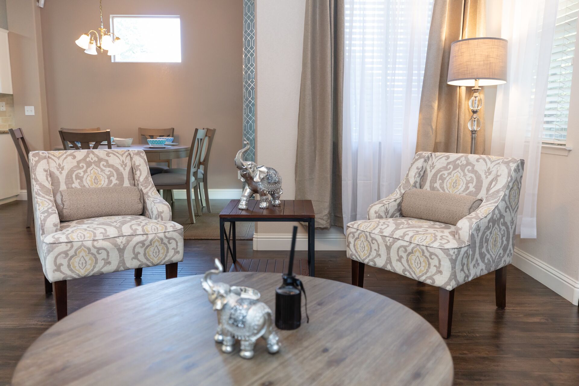 Un salon comprenant deux fauteuils à motifs, une table basse ronde ornée d’une statuette d’éléphant en argent, une petite table sur laquelle repose une sculpture d’éléphant en argent, et une lampe.