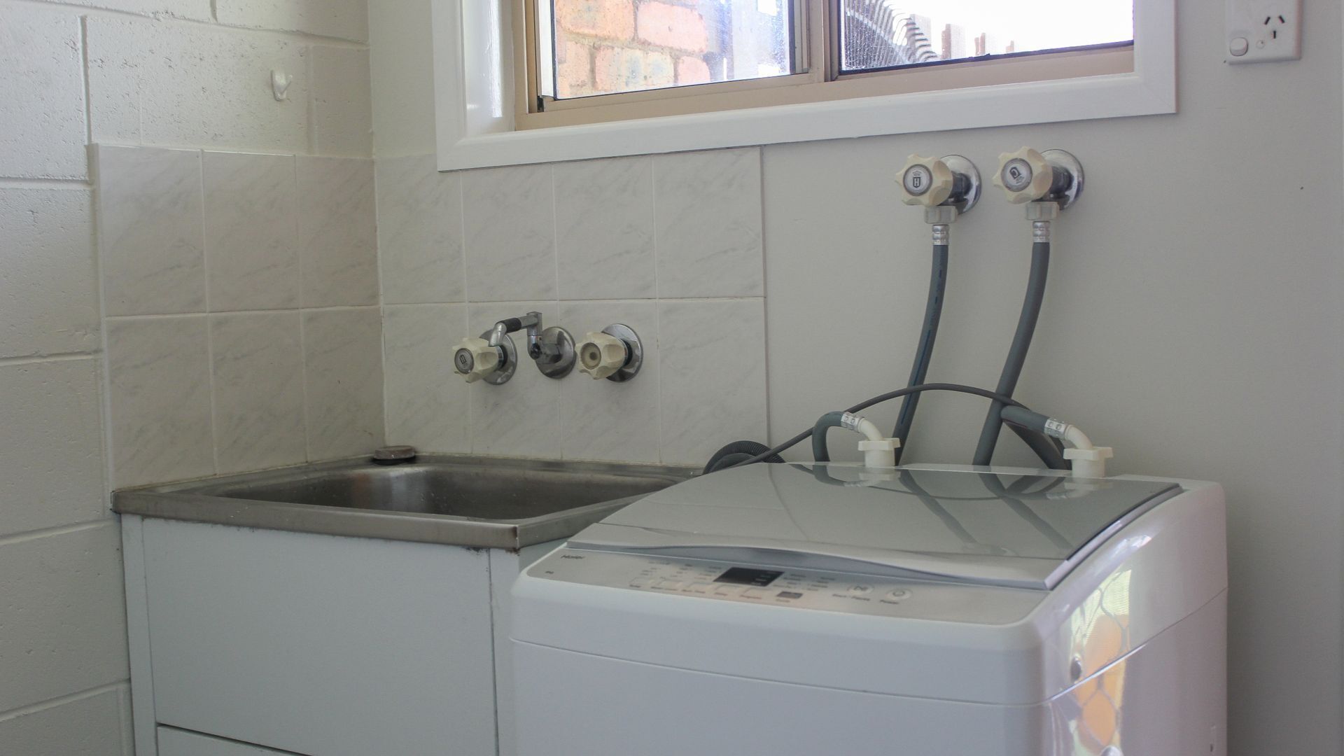 Een wasruimte met een wasbak, twee kraan en een wasmachine.