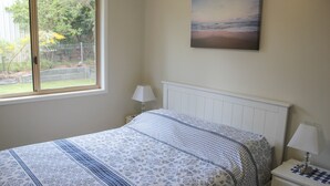 Ein Schlafzimmer mit Bett, Nachttisch, Fenster mit Blick ins Freie und einem Bild an der Wand.