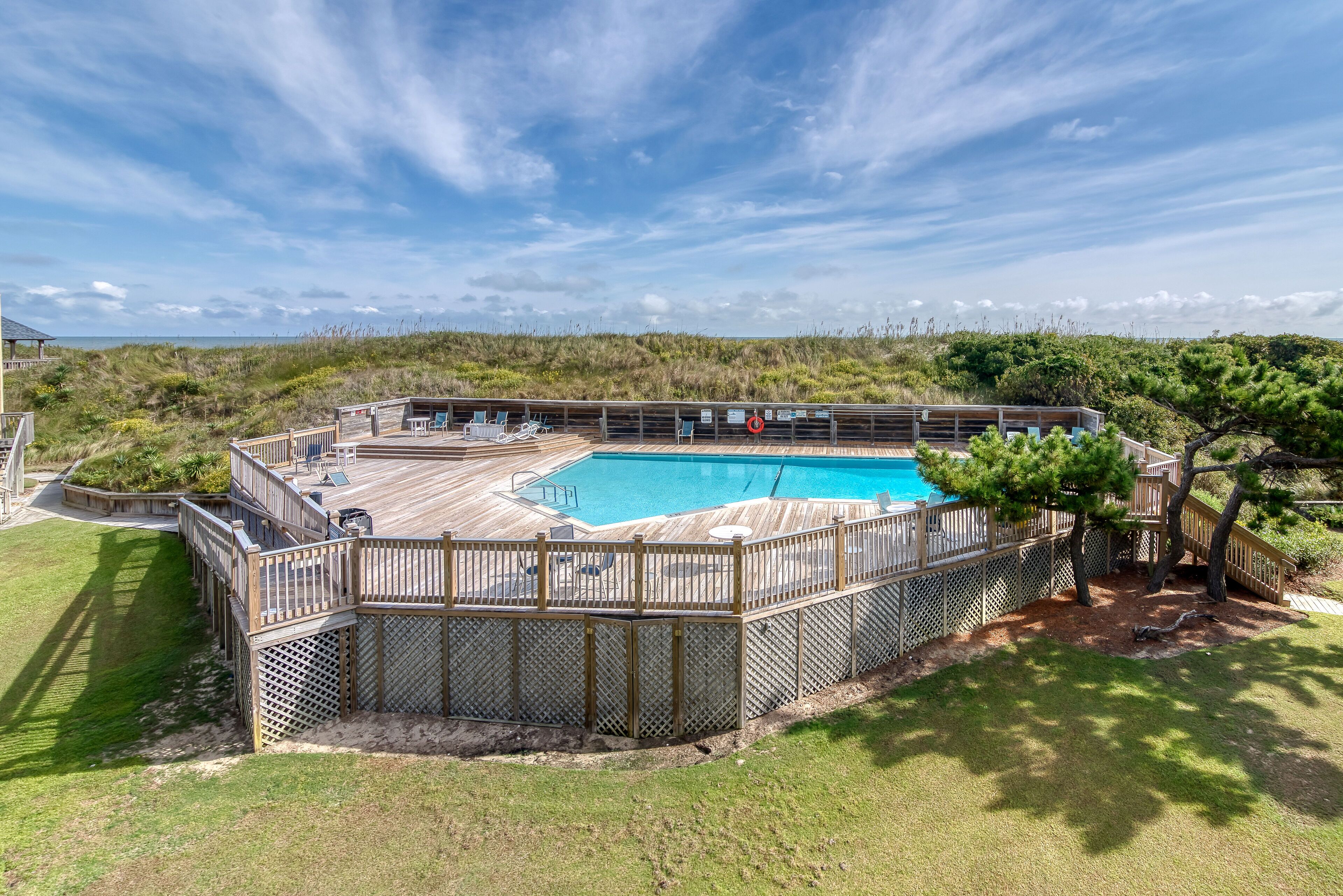 Um quintal com um deck de madeira, piscina e vista para a praia.