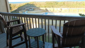 A wooden deck with two chairs and a small table, overlooking a pool and a grassy area.