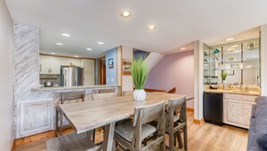 A modern kitchen with a wooden dining table, chairs, and a refrigerator.