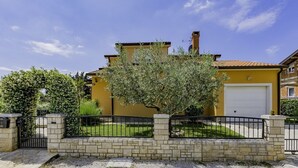 A yellow building with a white garage door, surrounded by a brick wall and a metal fence. - Apartment in a quiet location (Umag)