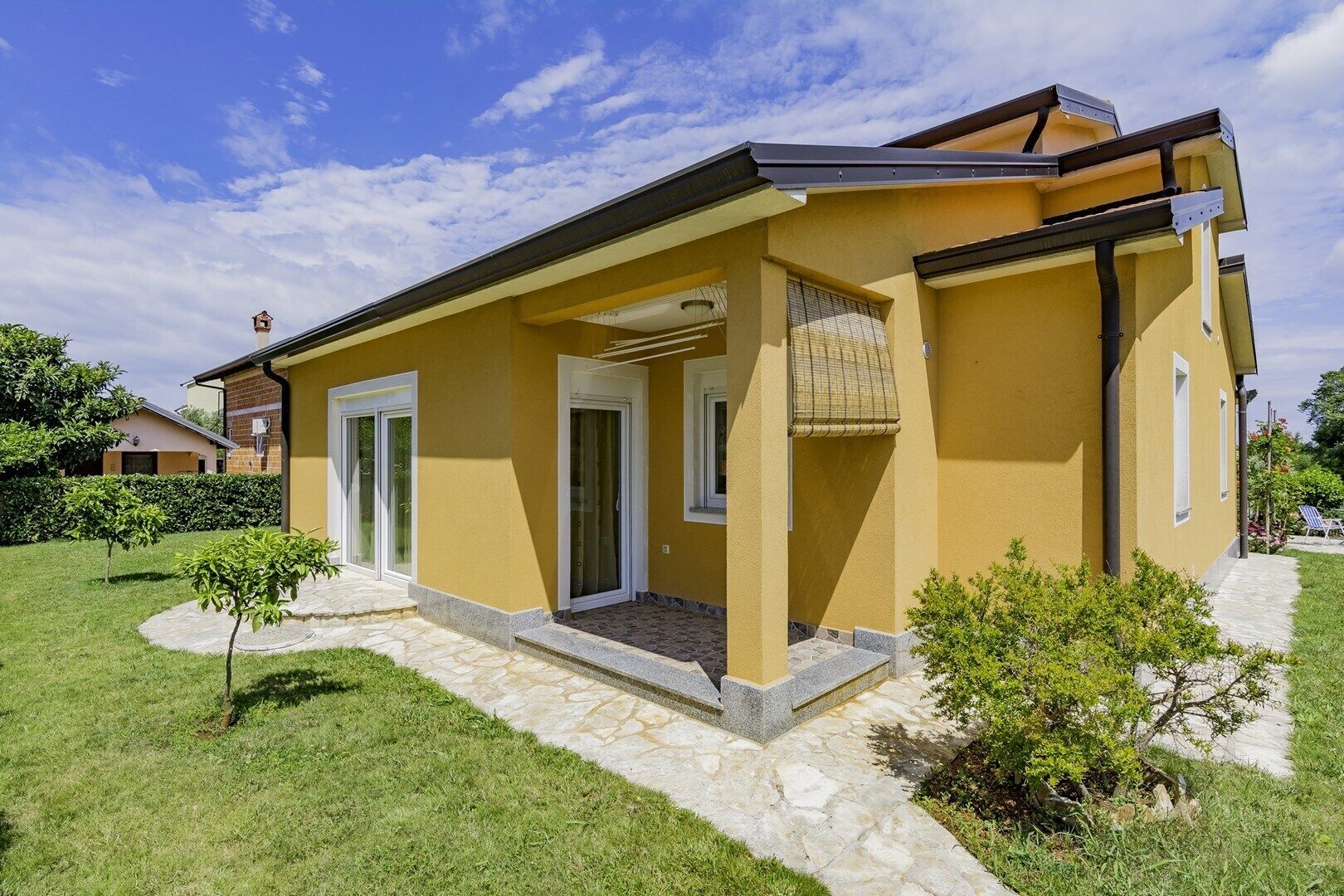 Een geel huis met een pad van stenen, een kleine tuin en een helderblauwe lucht.