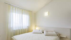 A neatly made bed with white linens and pillows, a bedside table with a lamp, and a window with sheer curtains. - Apartment in a quiet location (Umag)