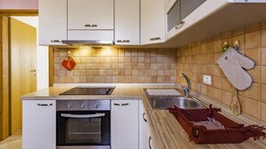 A kitchen with white cabinets, a stove, an oven, a sink, and a tiled backsplash. - Apartment in a quiet location (Umag)