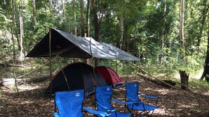 Una tienda de campaña con techo de lona, dos sillas de camping azules y una botella de agua sobre el suelo en un bosque.