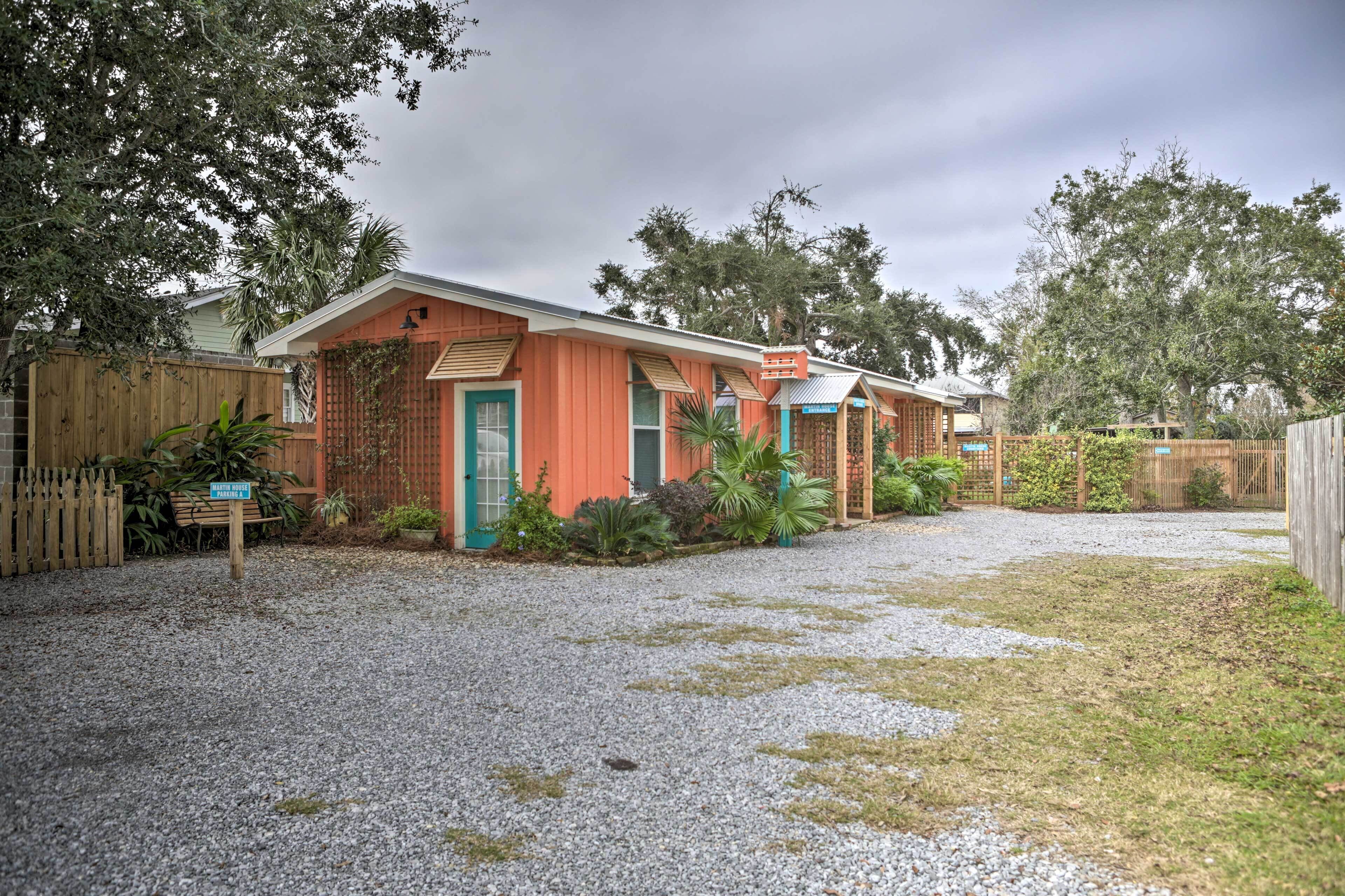 A two-story building with a red exterior and a green door, surrounded by a gravel driveway and a wooden fence.