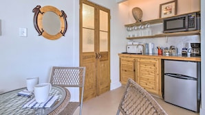 Cocina compacta con armarios de madera, microondas y refrigerador. Cuenta con un comedor con sillas de mimbre y una mesa de vidrio.