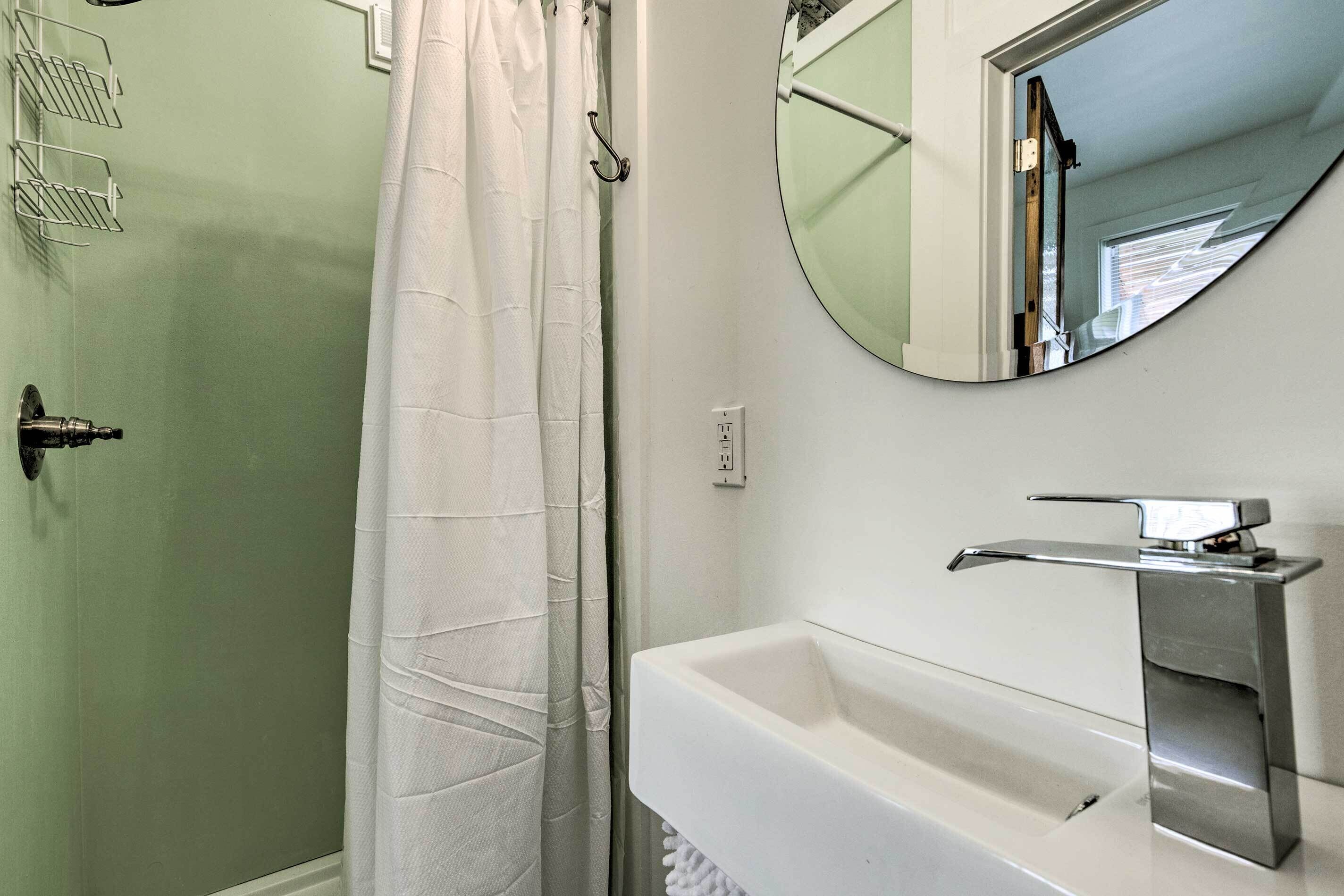 Un baño con ducha, lavamanos y espejo.