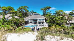 Una casa grande con piscina, rodeada de árboles y una playa de arena.