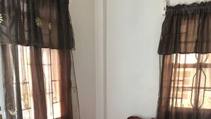 Un'area pranzo con un tavolo ricoperto da una tovaglia rossa, due sedie di legno e tende scure con motivi floreali.