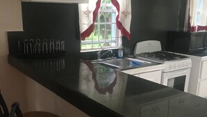 Una cucina con un piano di lavoro nero, mobili bianchi, un fornello e una finestra con tende rosse.