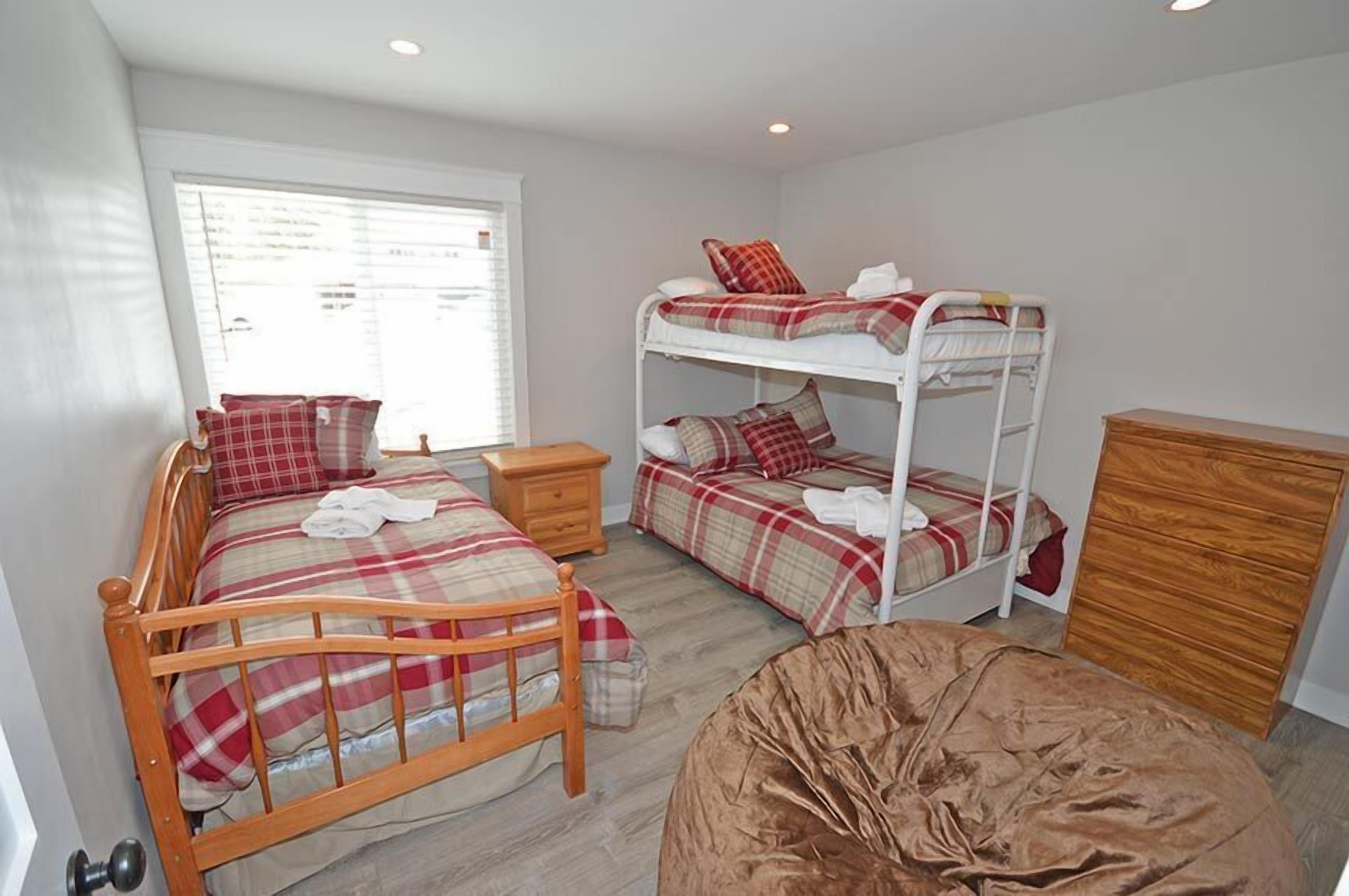 A bedroom with a wooden bed, a bunk bed, a wooden dresser, and a window with blinds.