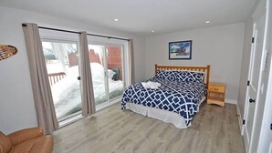 Ein Schlafzimmer mit einem Bett, einem Nachttisch aus Holz, einem Sessel und einer Schiebetür zum Balkon.