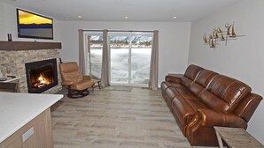 Ein modernes Wohnzimmer mit Kamin, Ledersofa und großem Fenster mit Blick auf schneebedeckte Berge.