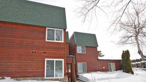Ein zweigeschossiges Holzhaus mit grüner Dachdeckung, einem Steinfundament und verschneitem Gelände.
