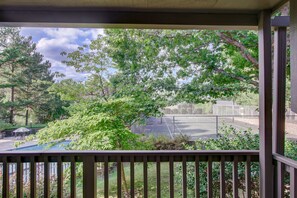 Relax in a serene outdoor space surrounded by lush greenery and trees, with a view of the tennis court.