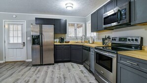 A modern kitchen with dark cabinets, stainless steel appliances, and a wooden countertop.