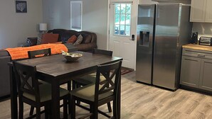 A modern kitchen with stainless steel appliances, a dining area with dark wood furniture, and a living room with a sofa and cushions.