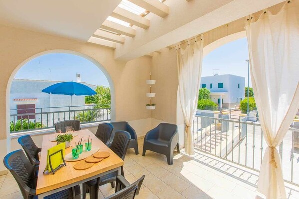 A balcony with a table and chairs, a blue umbrella, and a view of buildings and greenery.