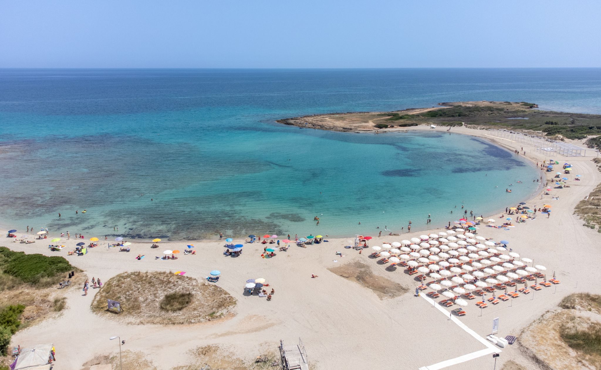 A beach with clear turquoise waters, a sandy shore, and numerous umbrellas.