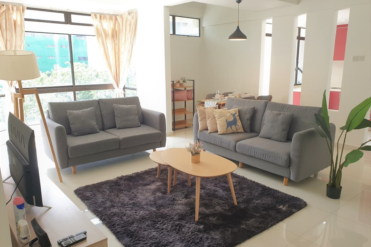 A living room with two grey sofas, a coffee table, a TV, and a large window with curtains.