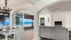 A spacious living area with a view of the beach, a dining area with a table set for two, and a modern grey sofa. - Villa Mer Vue (Madampagama)