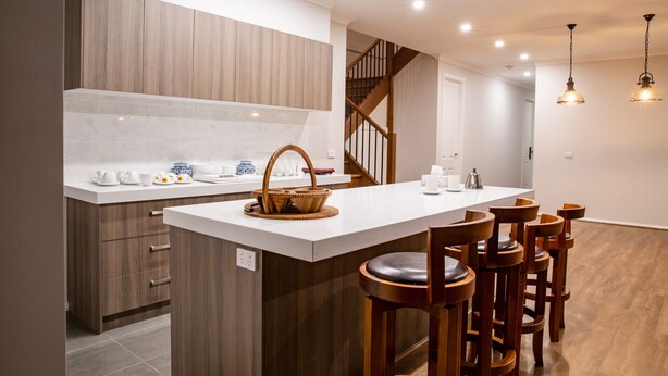 A modern kitchen with wooden cabinets, a white countertop, and a built-in island with stools.
