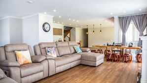 A spacious living room with a large sectional sofa, wooden flooring, and a dining area with wooden chairs and a table.