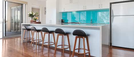 A modern kitchen with a central island, bar stools, and a refrigerator.