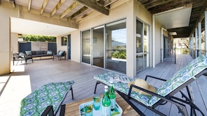 Une terrasse extérieure avec un canapé, des fauteuils, une table avec des boissons et une vue à travers des portes vitrées.