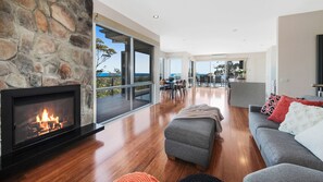 A modern living room with a stone fireplace, a grey sofa, and a view of the ocean.